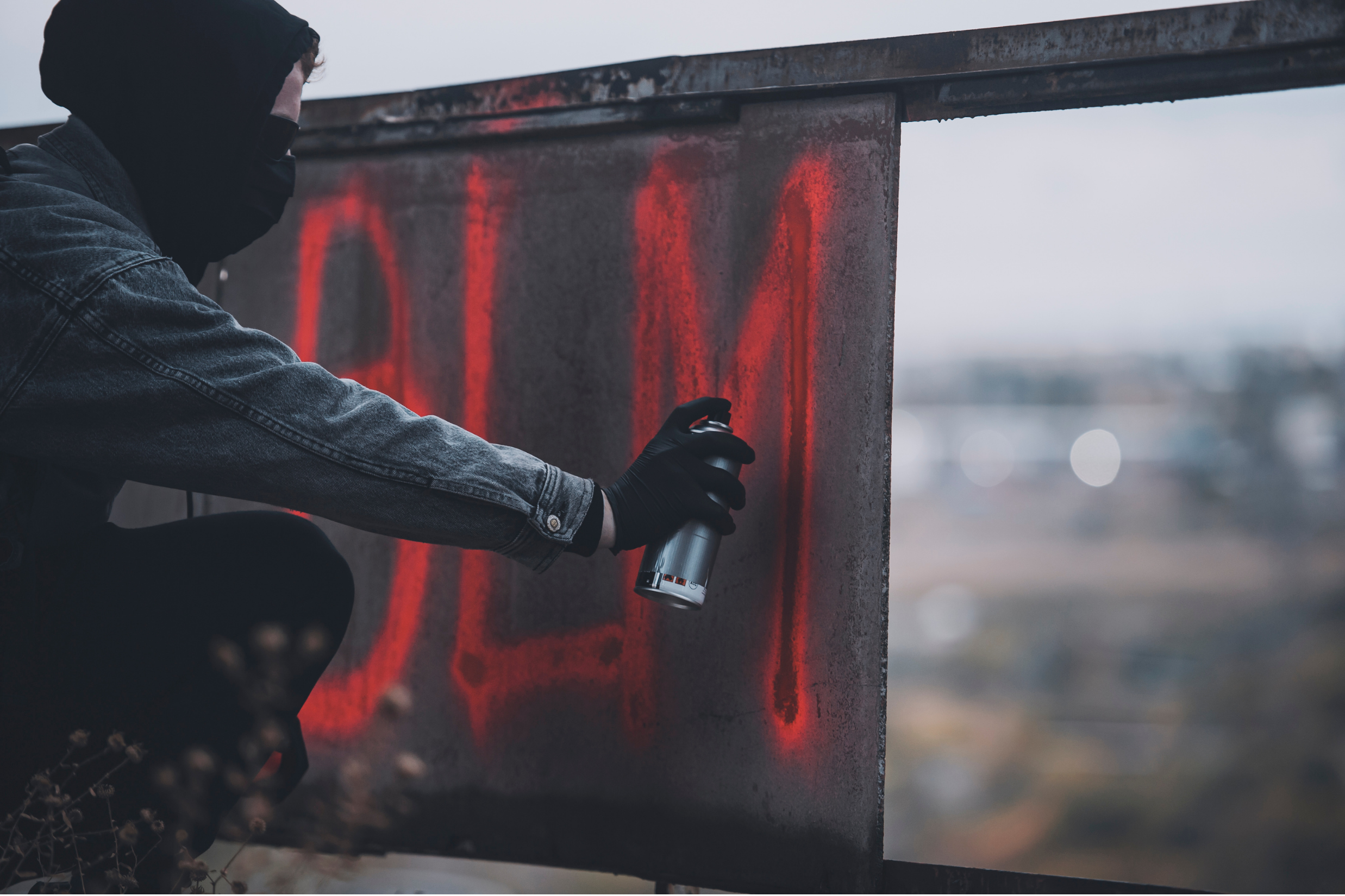 Hooded person spray painting graffiti on a metal surface, representing property damage from vandalism covered by insurance claims