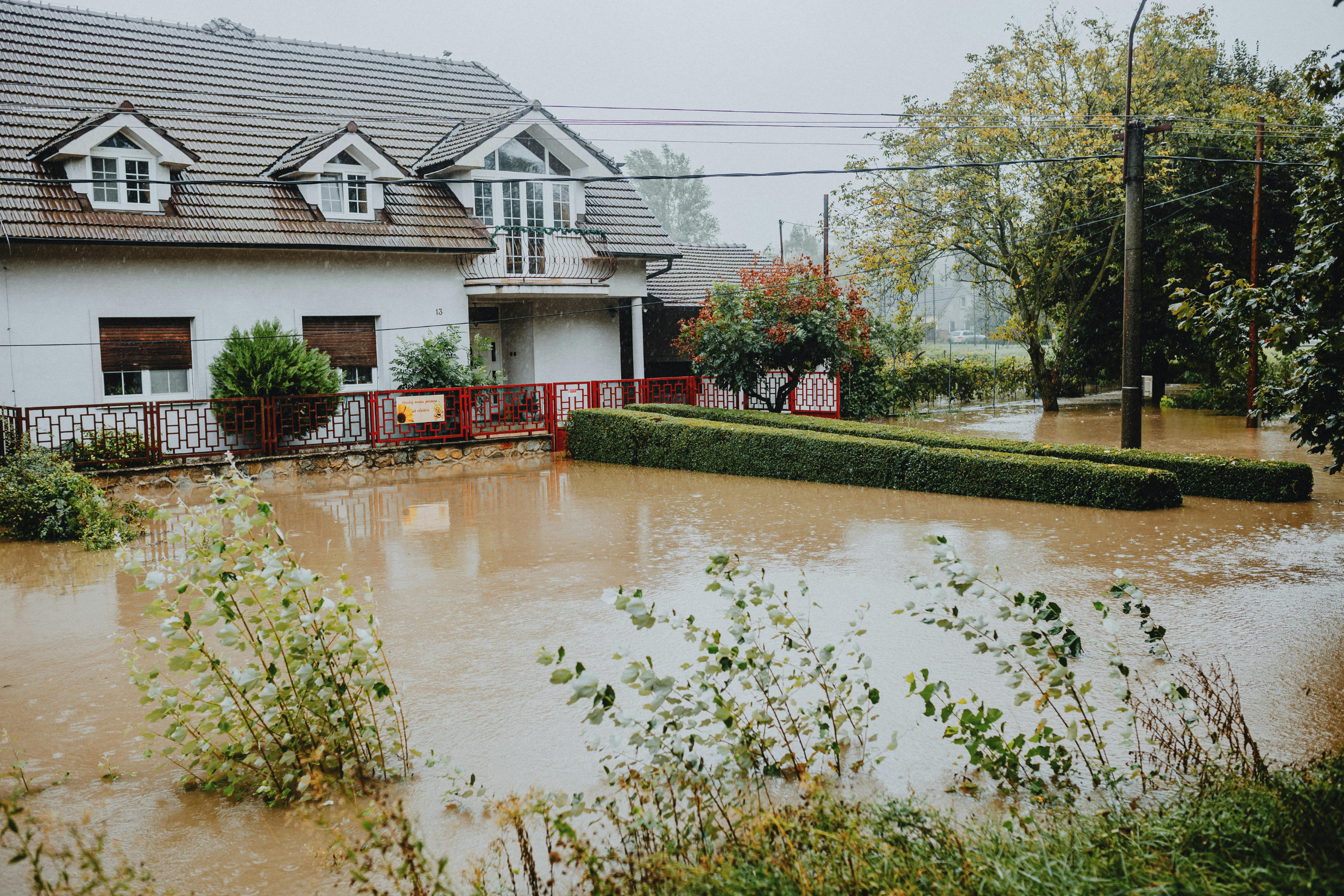 Flooded residential house with muddy water covering the yard after heavy rainfall, showing severe water damage